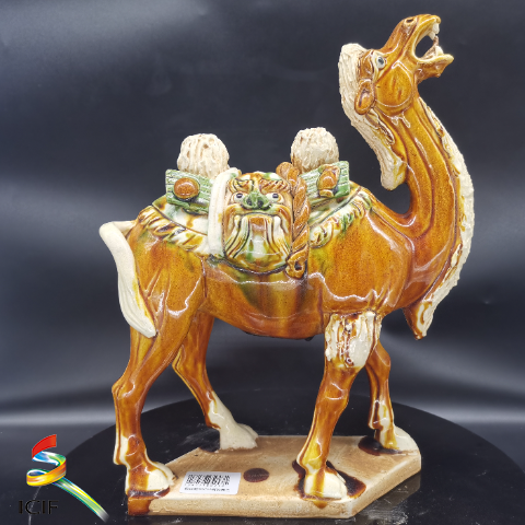 唐三彩载丝驼  展品介绍：此骆驼曲颈昂首，口鼻皆张，作嘶鸣状，立于长方形踏板之上，背部披黄绿白三色圆形垫子，双峰之间横搭装满物品的袋囊，两端有虎头。架上载有成卷的丝绸，系有飞禽野兔等物。该作品充分展示了创作者高超的艺术表现能力，在保持文物真品原貌的基础上，在作品的形式与内涵上均实现了新的突破，具有极高的观赏收藏价值。.png